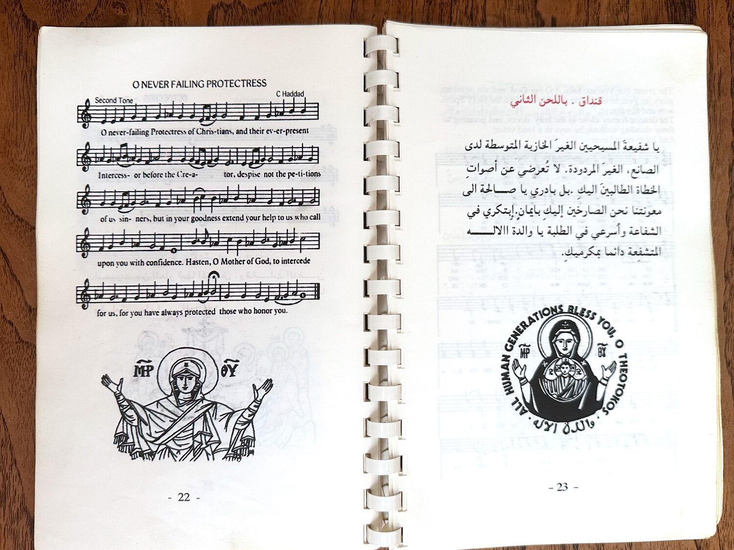 The liturgy booklet open to the hymn O Never-Failing Protectress, in English with musical notation, beside the same hymn in Arabic